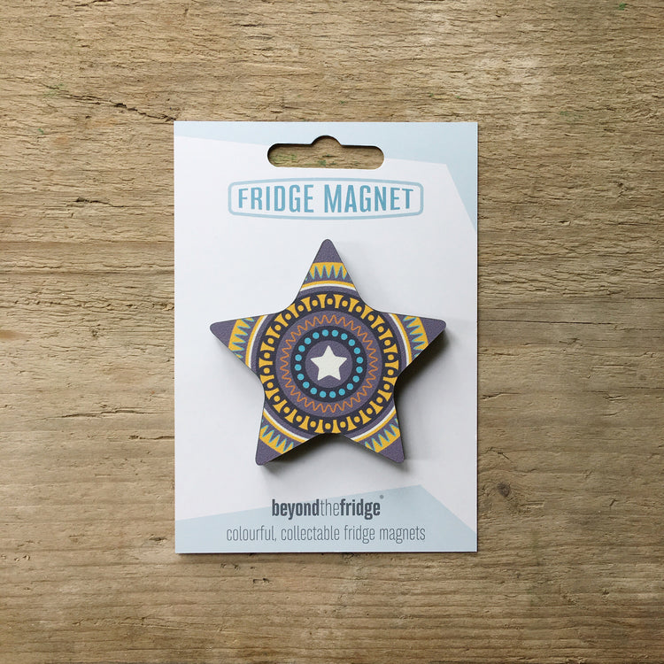 A purple star design plywood fridge magnet by Beyond the Fridge in it’s pack on a wooden background