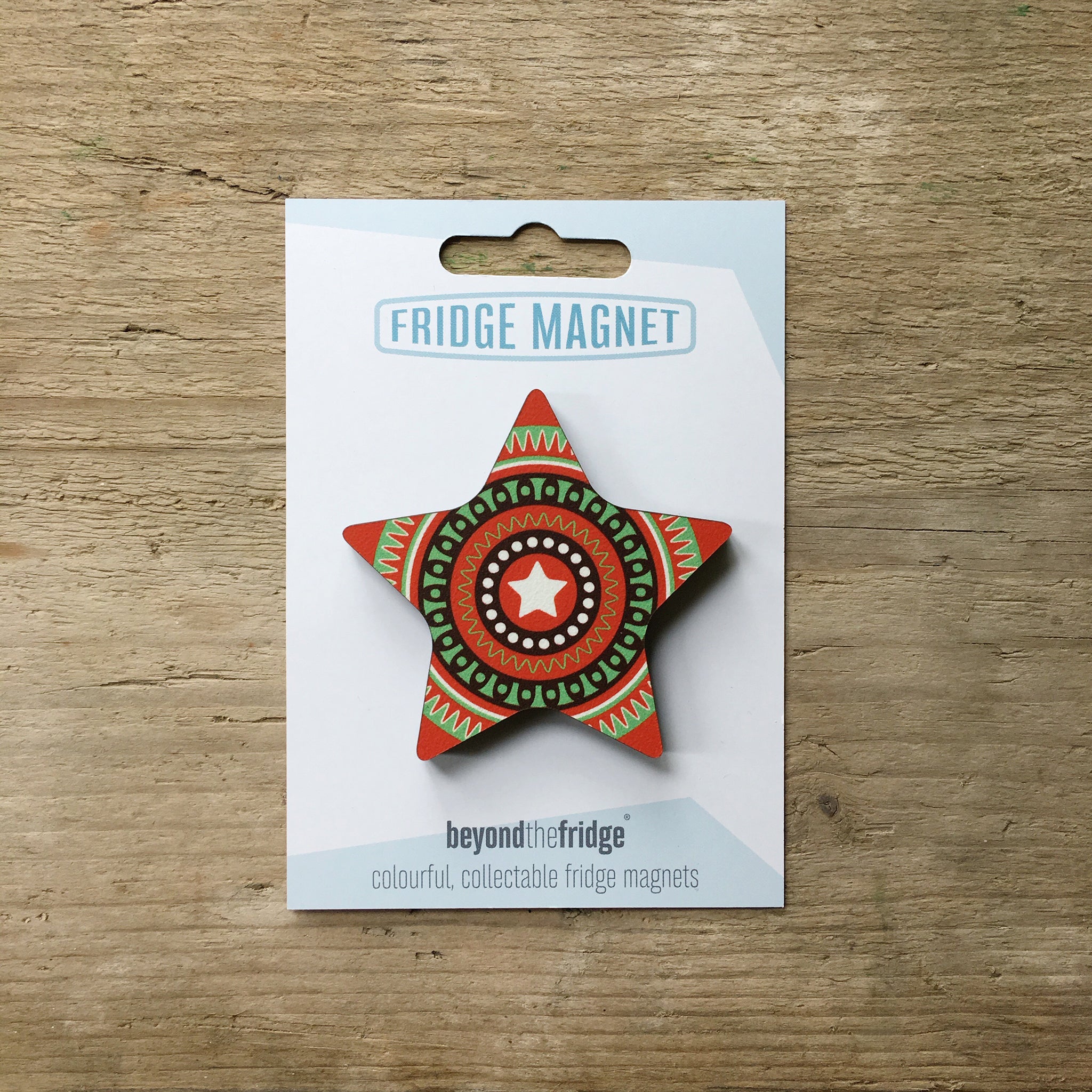 A red star design plywood fridge magnet by Beyond the Fridge in it’s pack on a wooden background