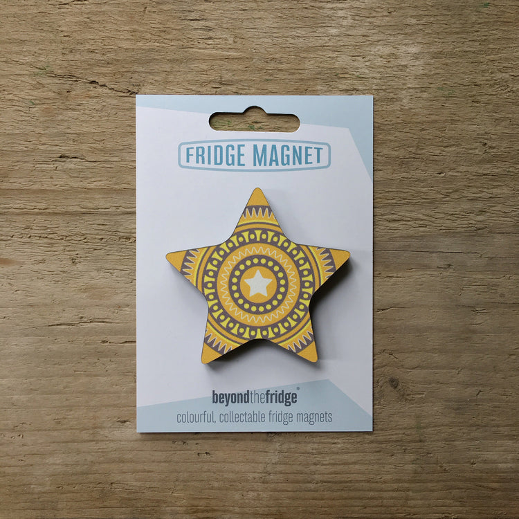 A yellow star design plywood fridge magnet by Beyond the Fridge in it’s pack on a wooden background