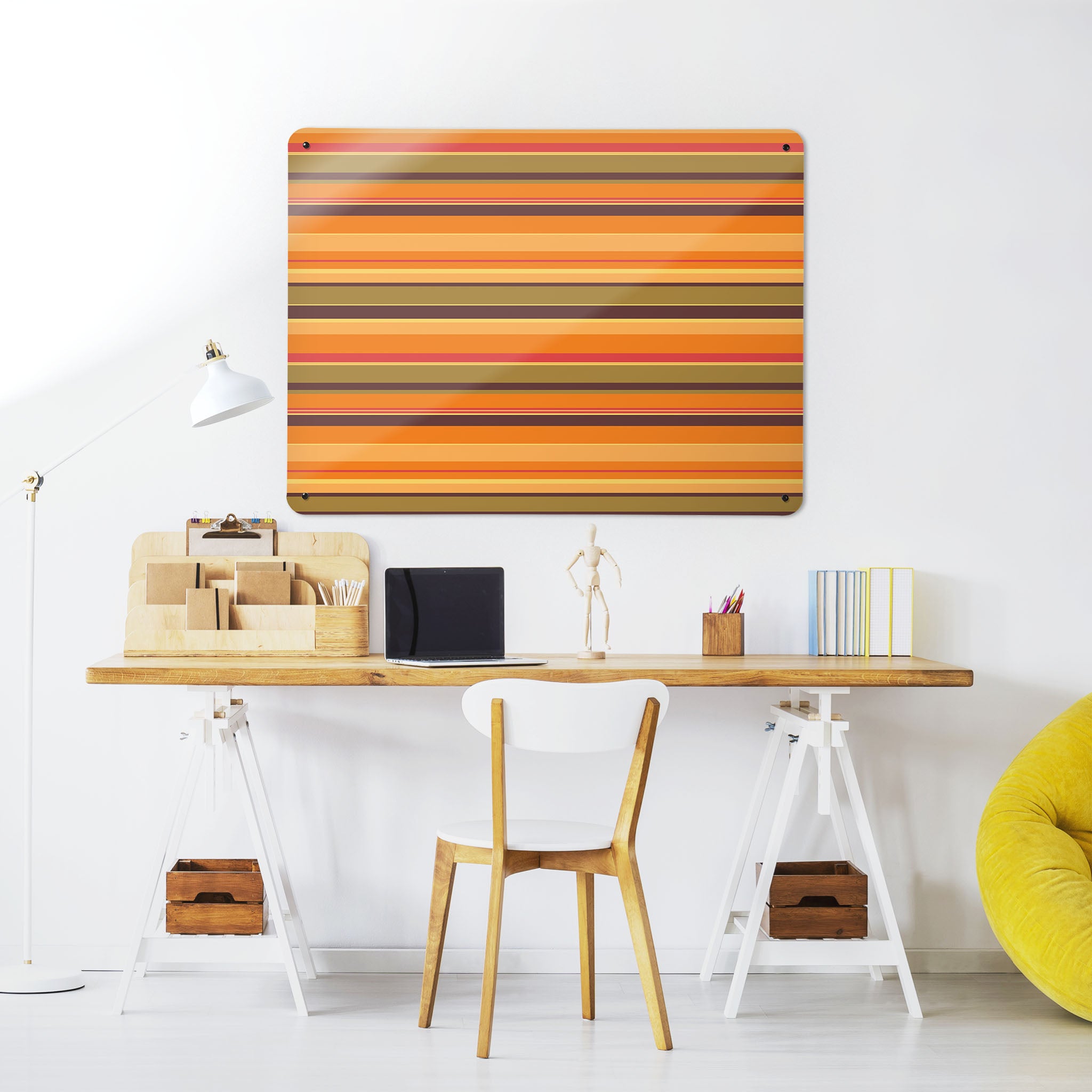 A desk in a workspace setting in a white interior with a magnetic metal wall art panel showing a stripes design in  pumpkin colours