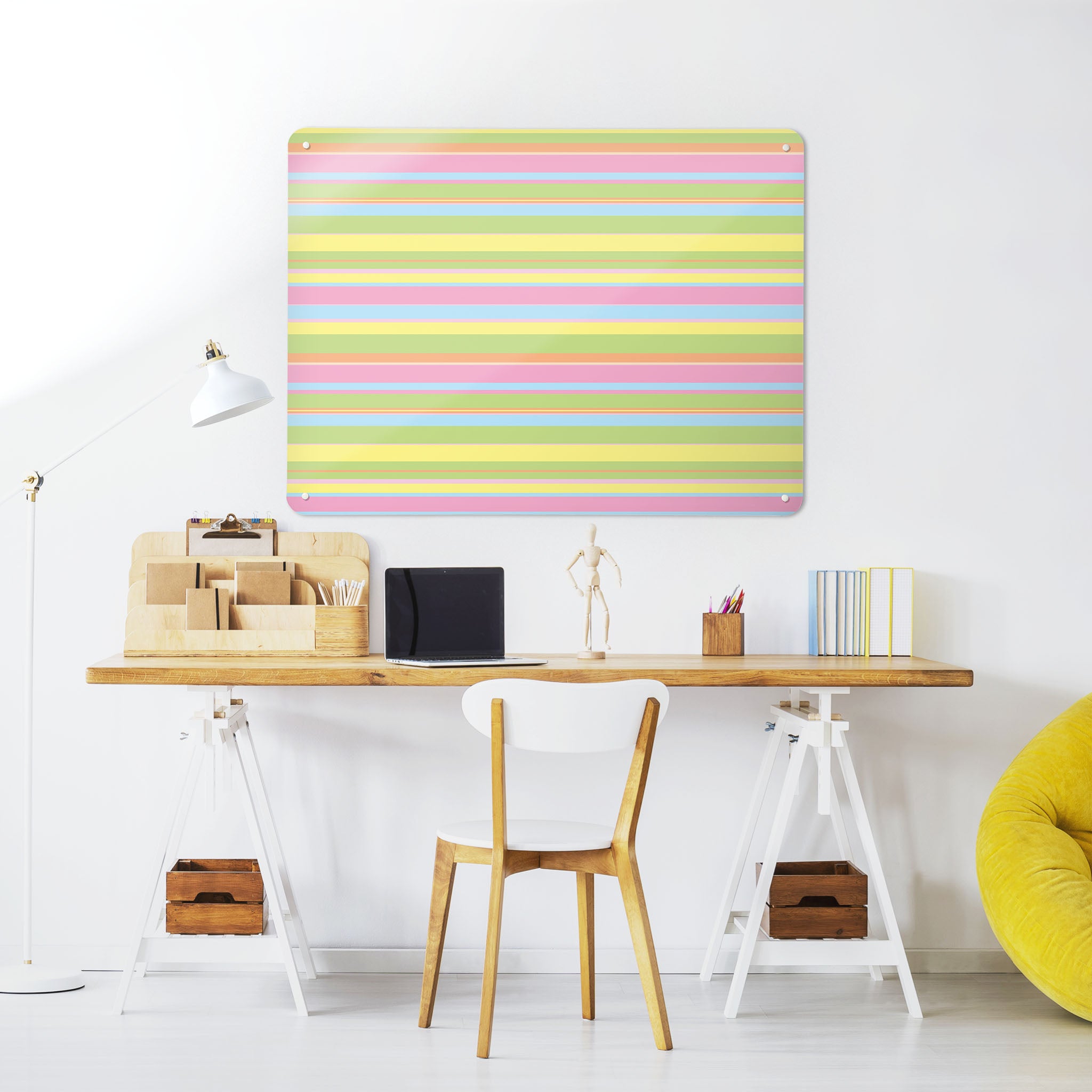 A desk in a workspace setting in a white interior with a magnetic metal wall art panel showing a stripes design in  candy colours