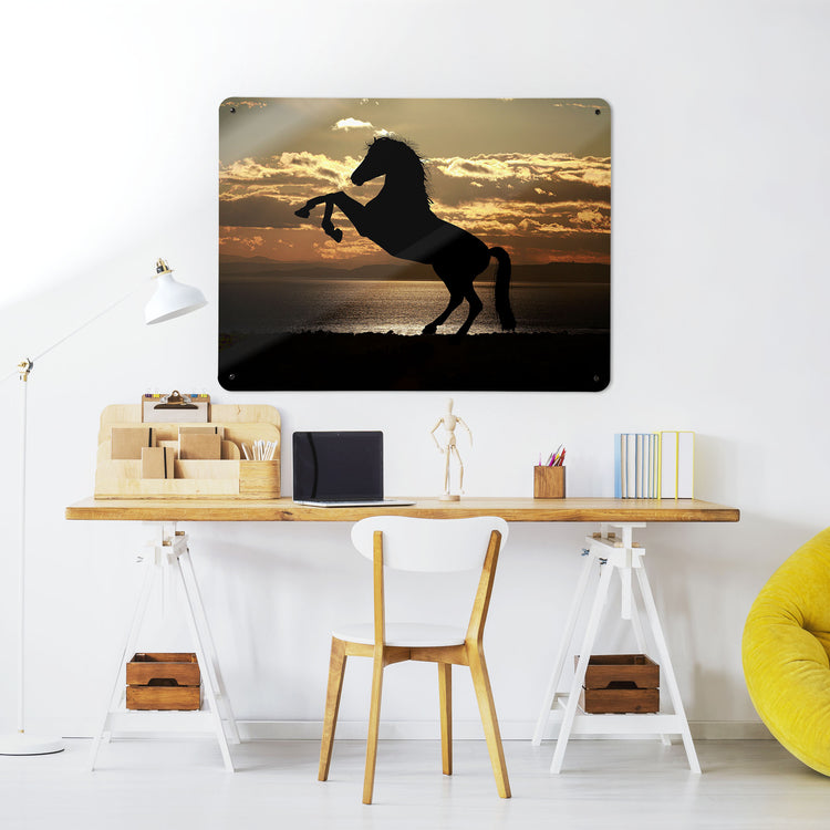 A desk in a workspace setting in a white interior with a magnetic metal wall art panel showing a rearing horse silhouette on a sunset backdrop
