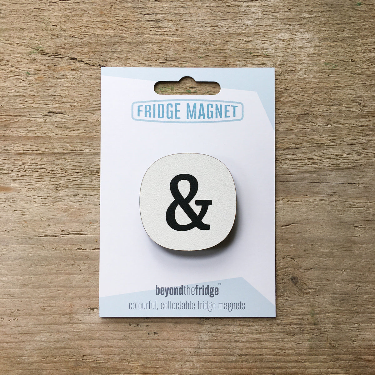 An ampersand fridge magnet in its Beyond the Fridge card packaging, on a wooden table