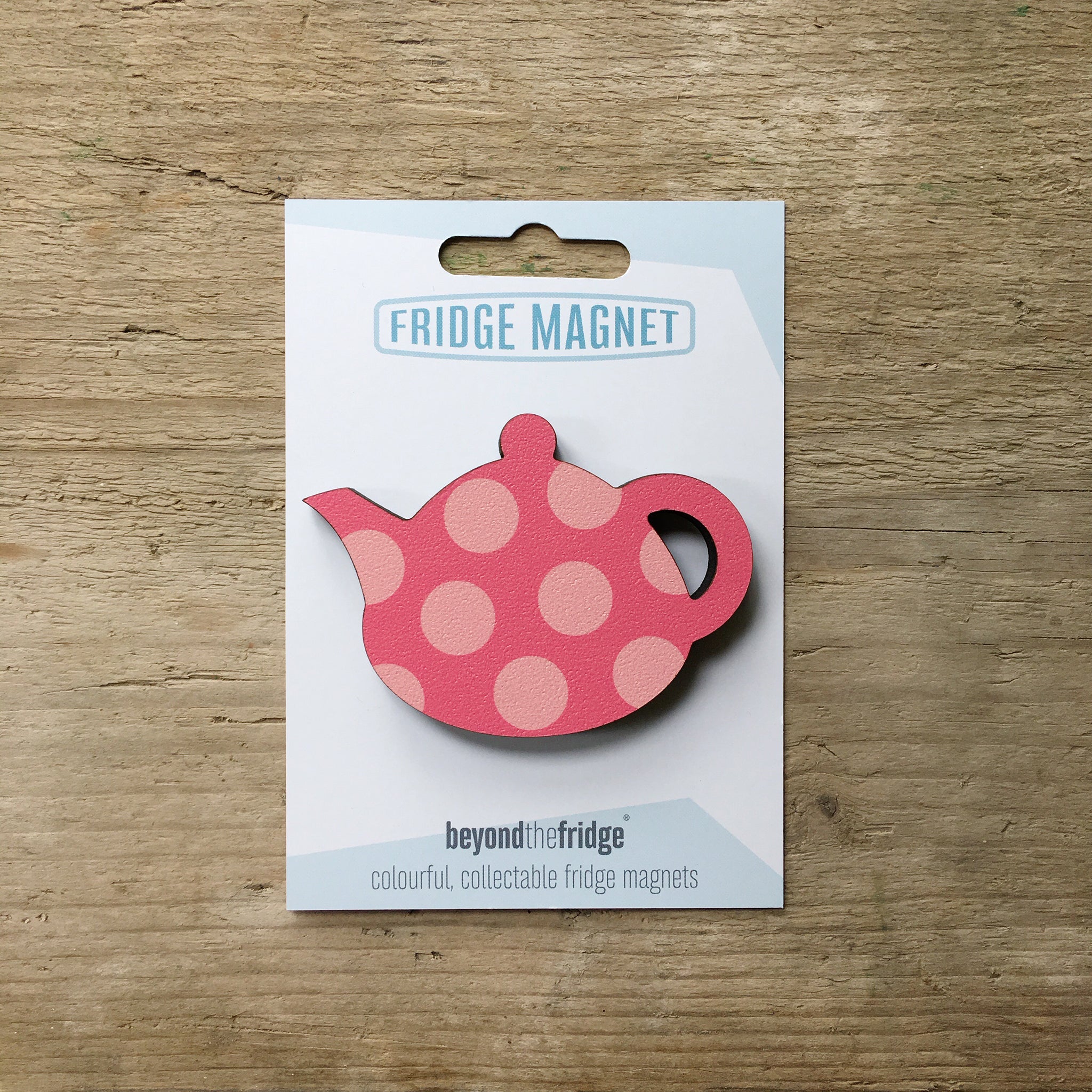A pink spotty teapot design plywood fridge magnet by Beyond the Fridge in it’s pack on a wooden background