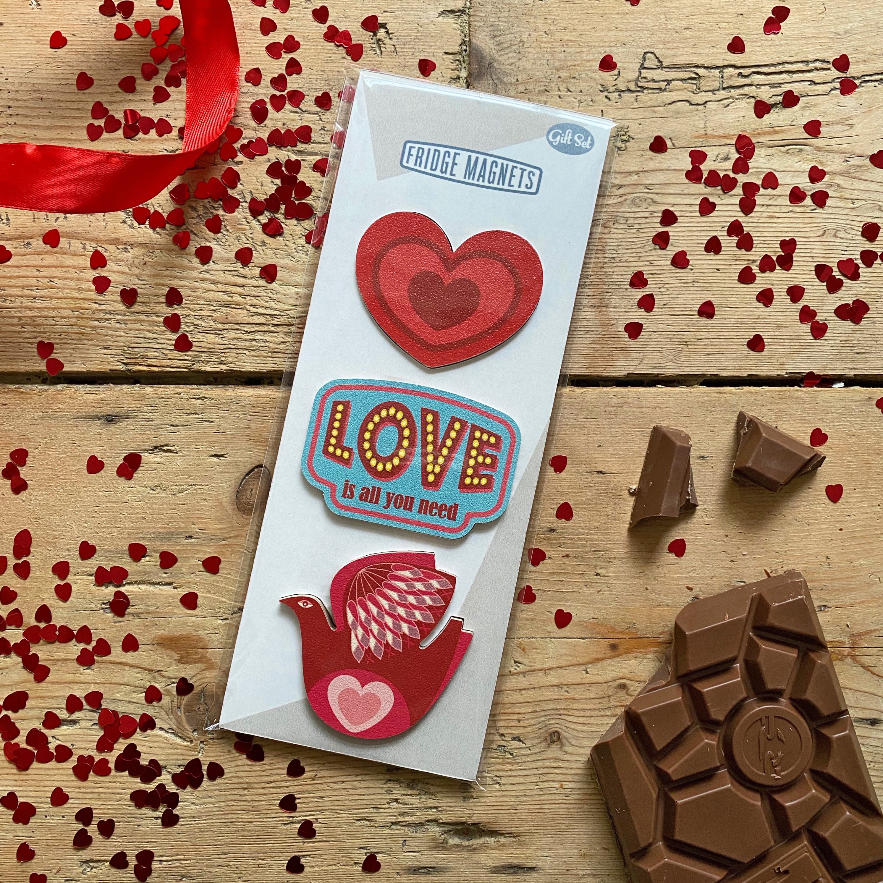 A gift set of three Fridge Magnets for Valentine's Day with heart, all you need is love vintage label and love bird magnets - by Beyond the Fridge on wood with chocolate and red ribbon