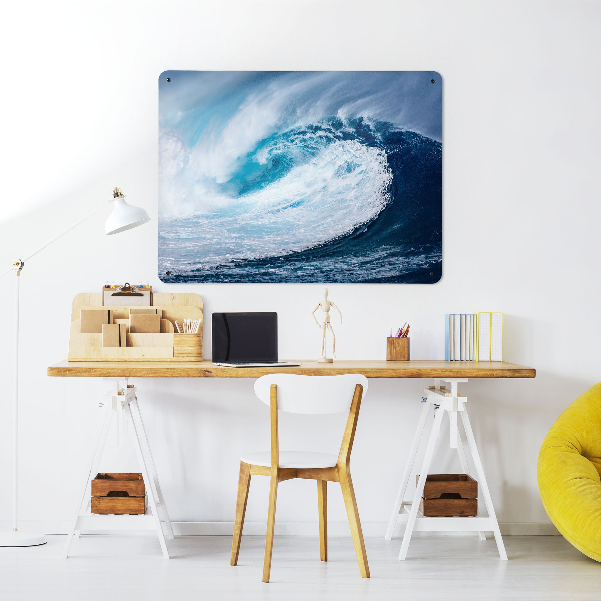 A desk in a workspace setting in a white interior with a magnetic metal wall art panel showing a photograph of a breaking wave