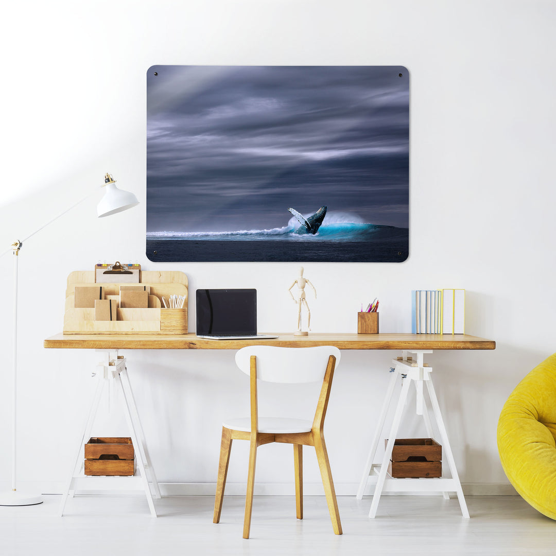 A desk in a workspace setting in a white interior with a magnetic metal wall art panel showing a photograph of a whale leaping out to sea