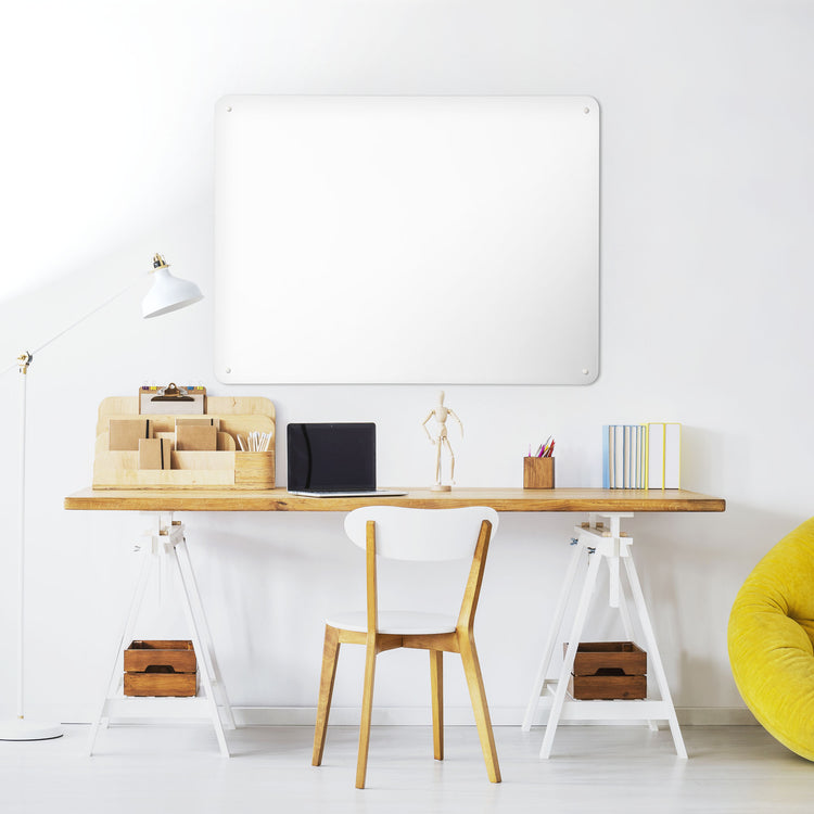 A desk in a workspace setting in a white interior with a plain white magnetic metal wall art panel 