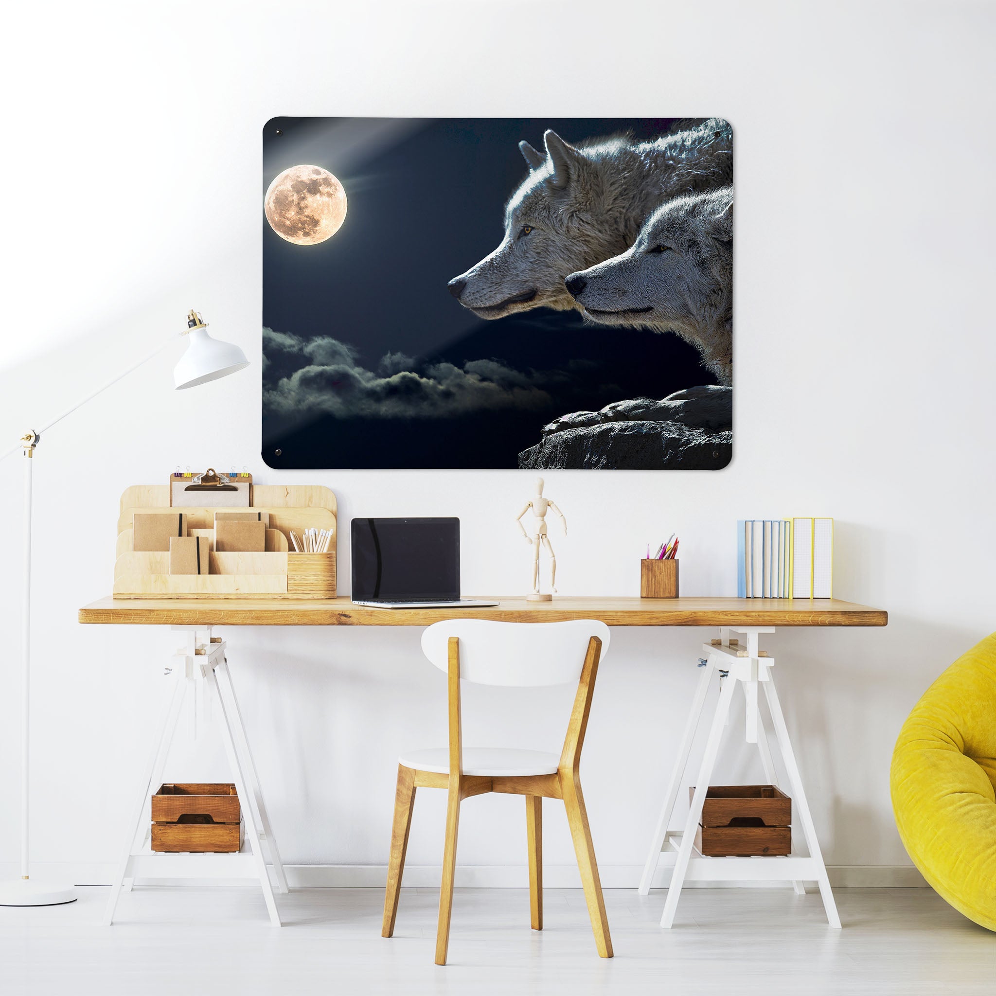 A desk in a workspace setting in a white interior with a magnetic metal wall art panel showing a photographic image of two wolves with a night sky and full moon