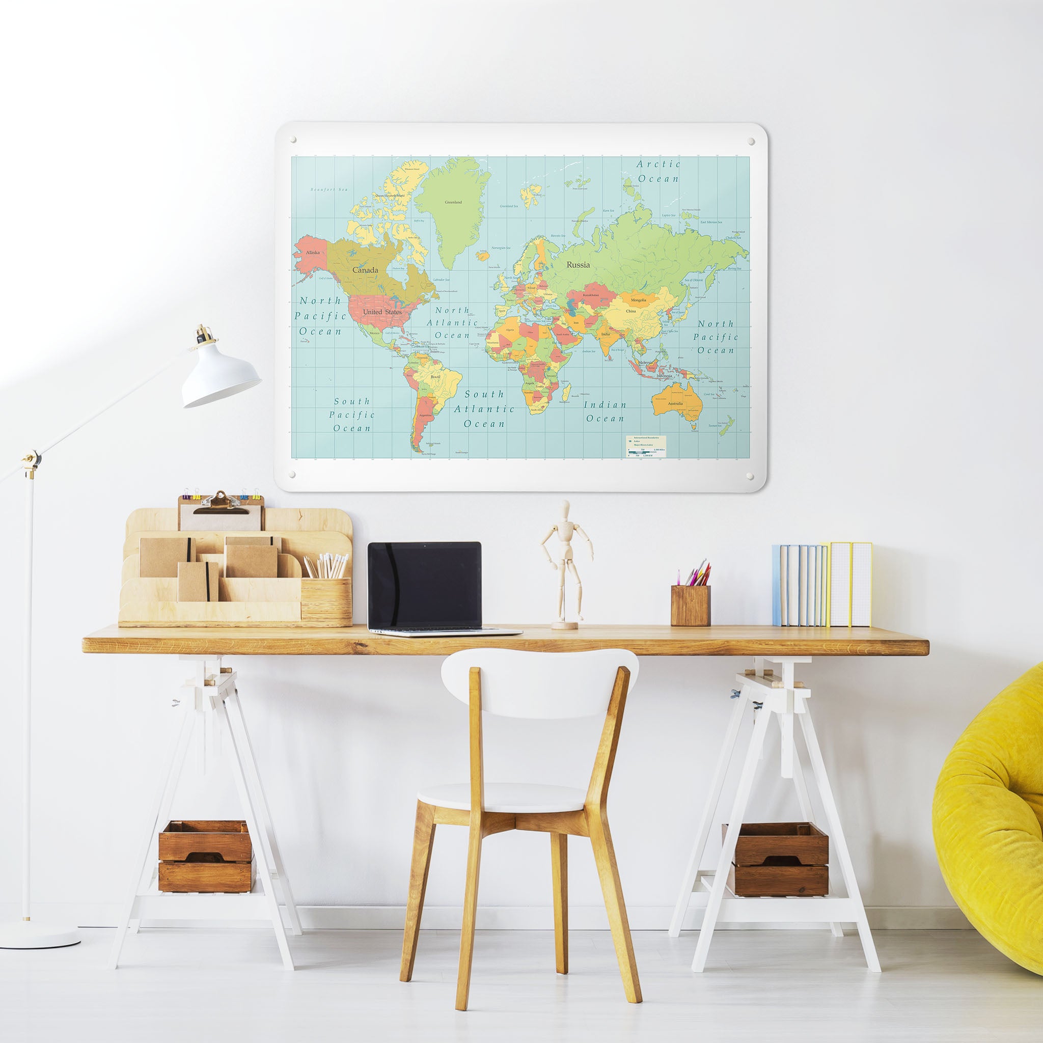 A desk in a workspace setting in a white interior with a magnetic metal wall art panel showing a world map design