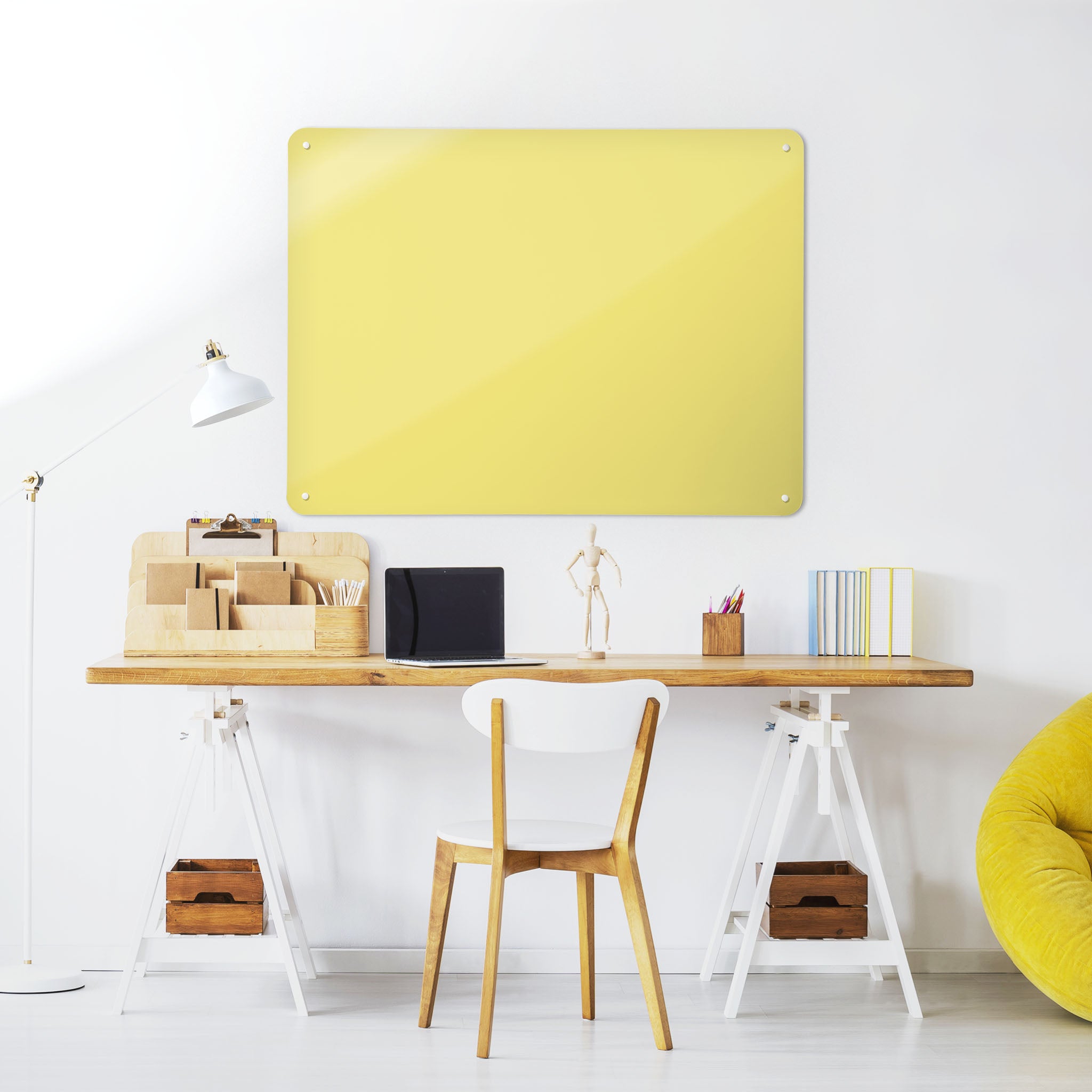 A desk in a workspace setting in a white interior with a plain yellow coloured magnetic metal wall art panel 