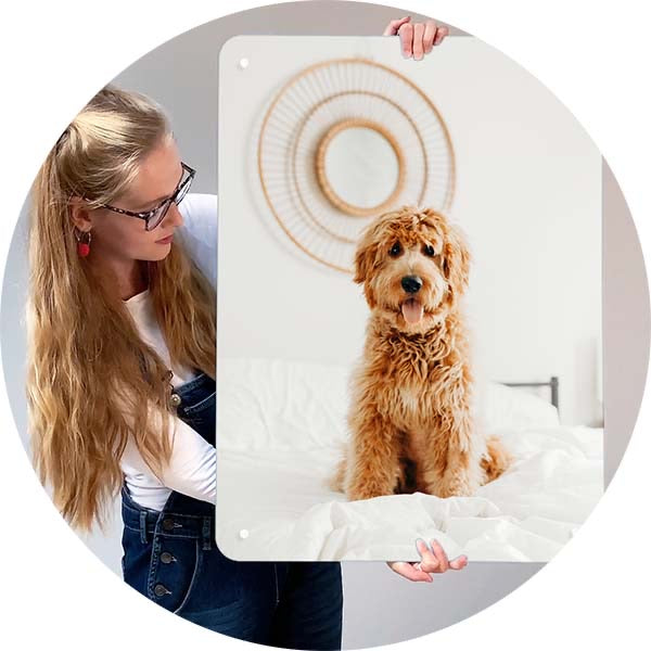 A woman holding up a magnetic board printed with her own photograph of a cockapoo sitting on a bed