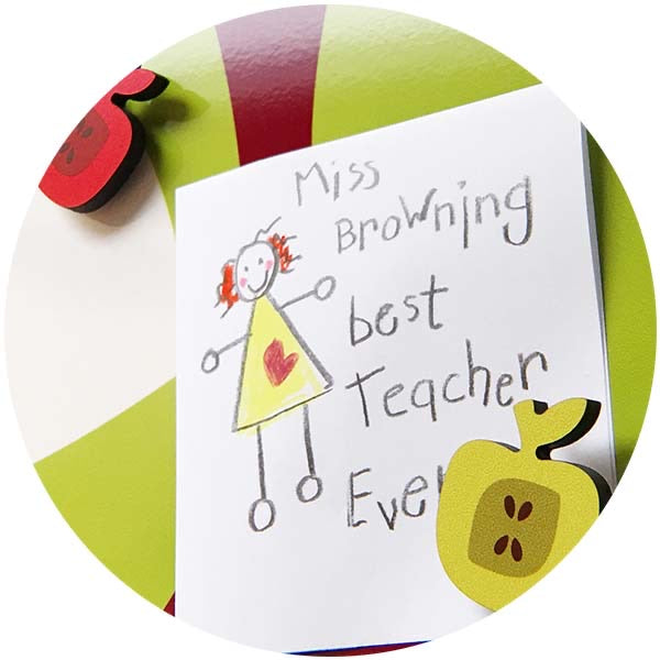 Apple-shaped fridge magnets holding a child's drawing captioned 'Miss Browning best teacher ever'