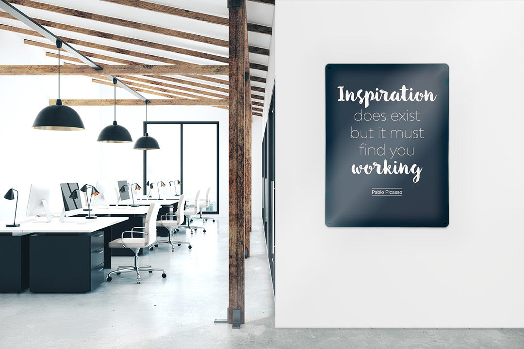A dark magnetic board printed with a Pablo Picasso quotation, on the wall of an open-plan office