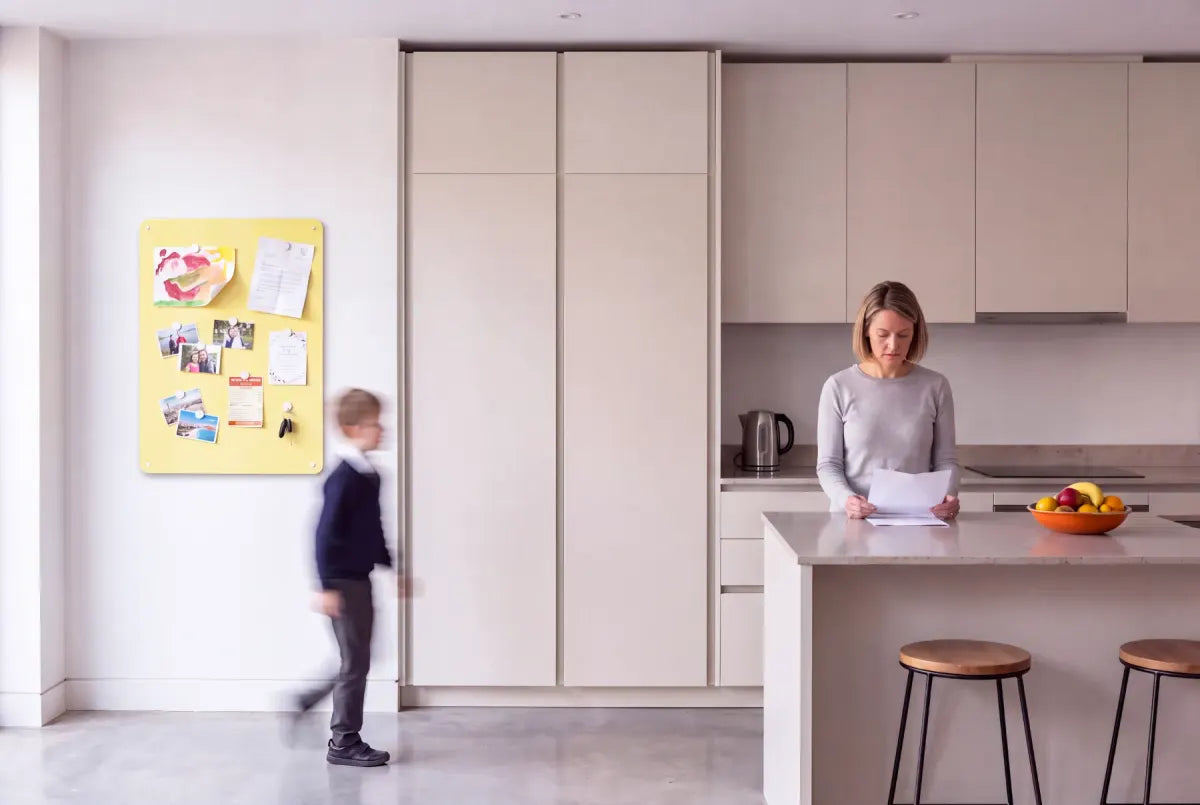 A plain yellow magnetic board beside the tall units of a fitted kitchen.