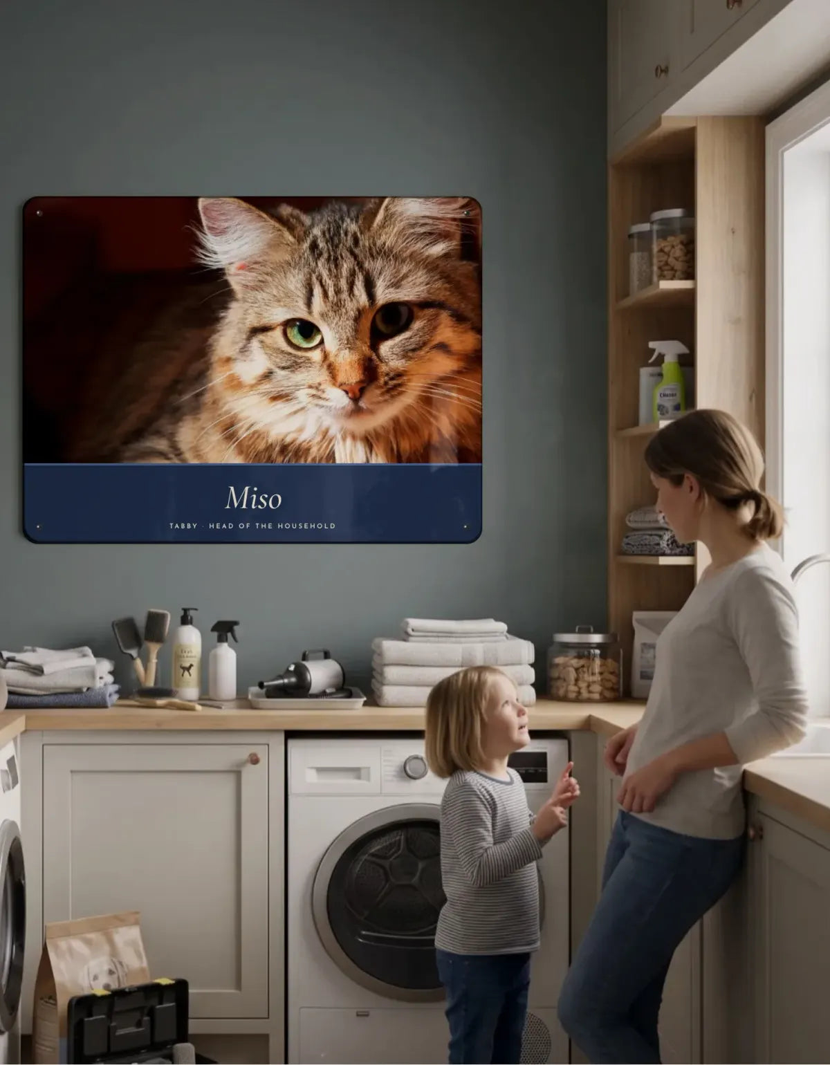 A portrait board of Miso the tabby cat on a utility room wall, with a mother and her daughter looking up at it.