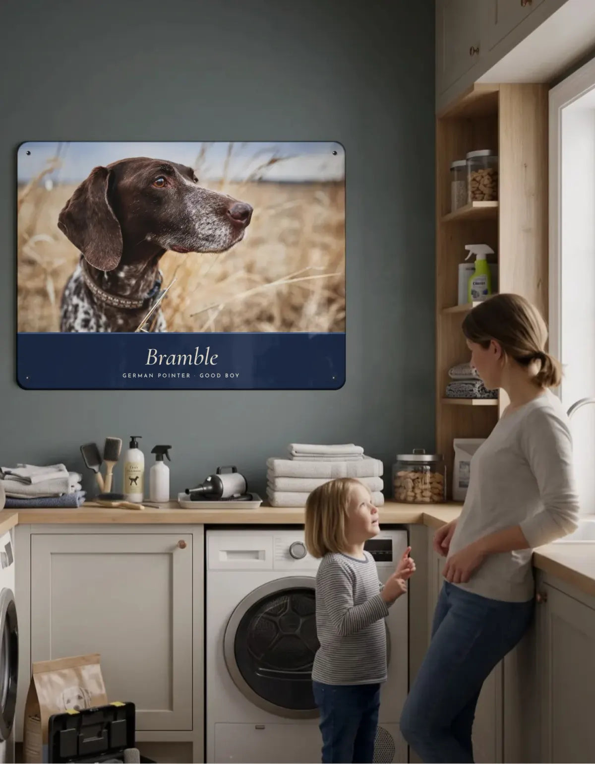 A portrait board of Bramble the German pointer on a utility room wall, with a mother and her daughter looking up at it.
