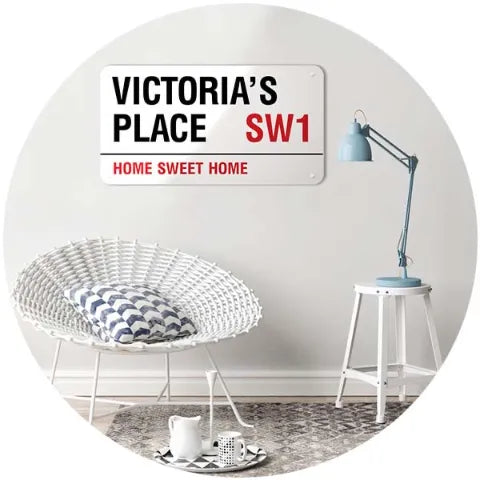 A personalised sign reading Victoria’s Place SW1, Home Sweet Home, on a wall above a cane chair and lamp